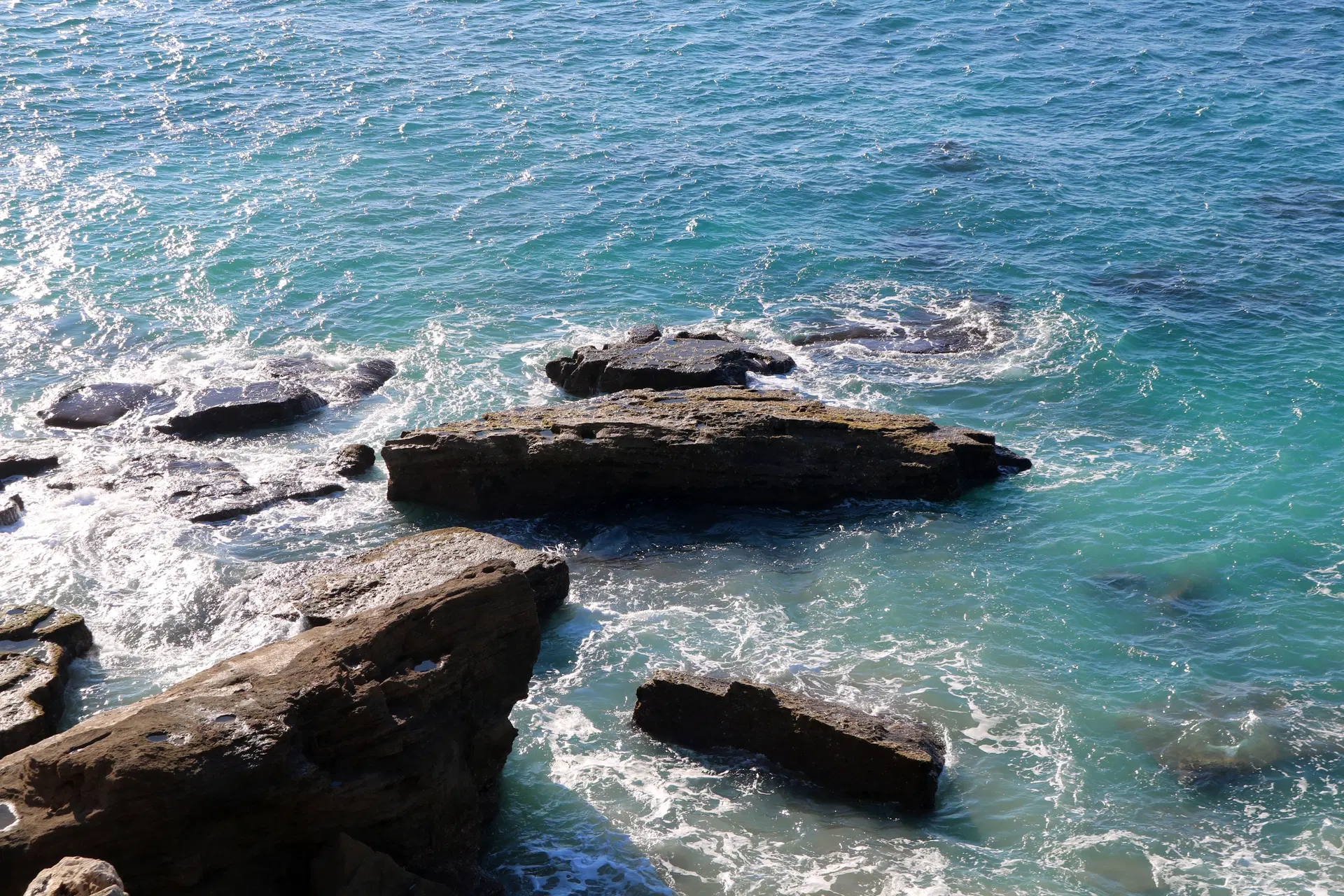 Rocky shoreline with turquoise sea waves flowing around large coastal rocks.