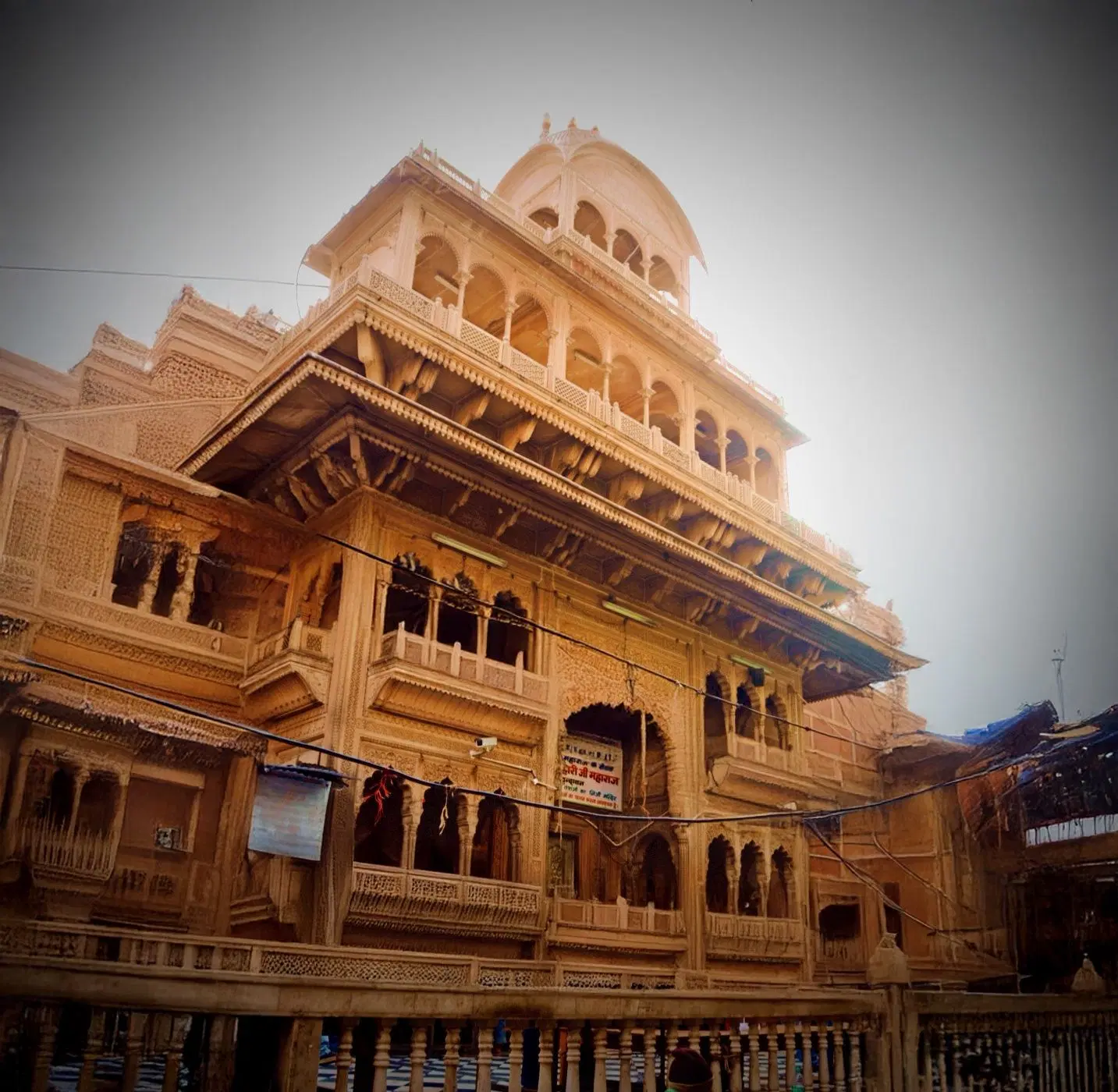 Traditional temple architecture with carved stone walls, arched balconies and domes in warm sunlight.