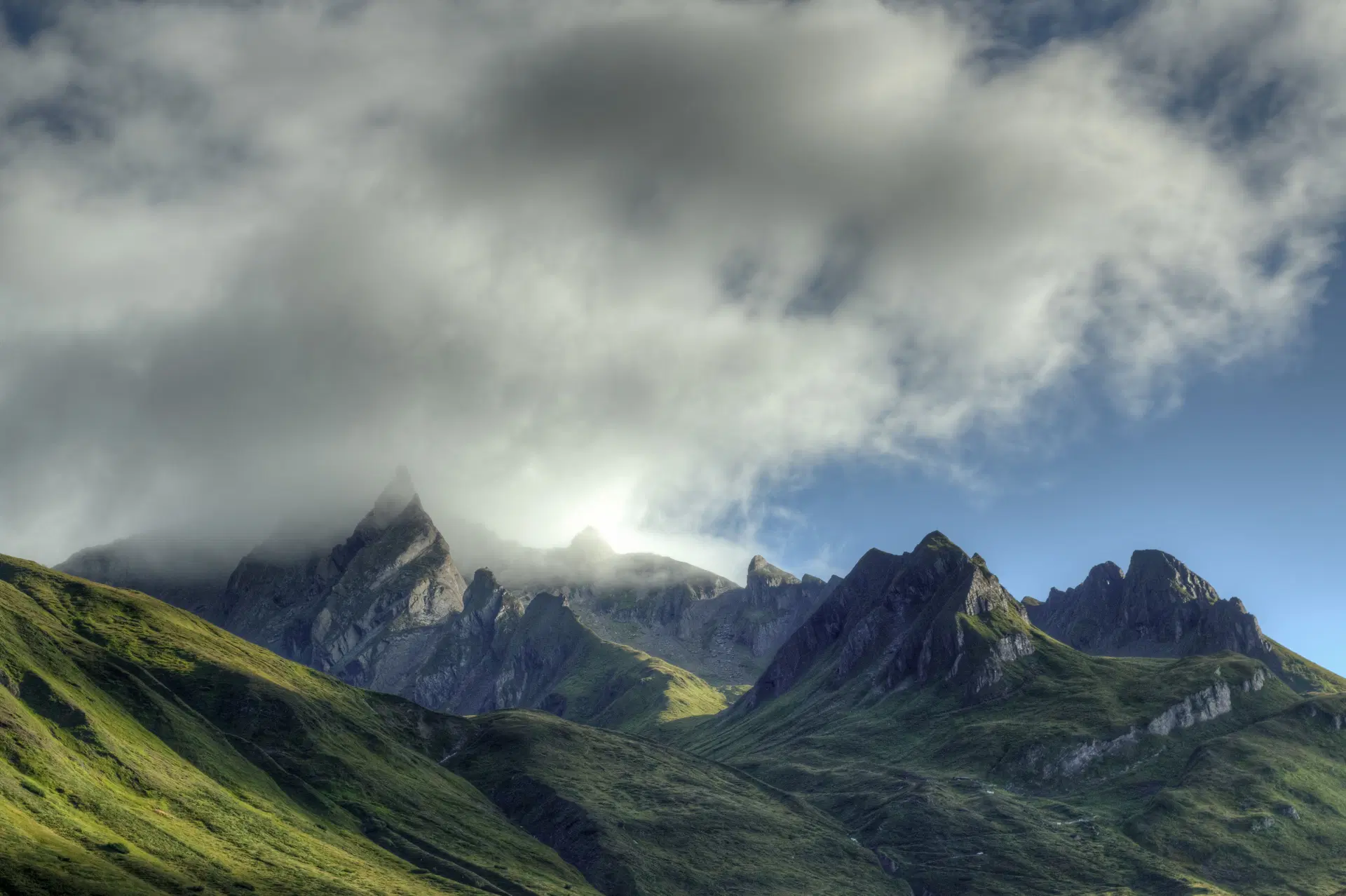 Green mountain landscape with rocky peaks, rolling hills and thick clouds covering the sky.