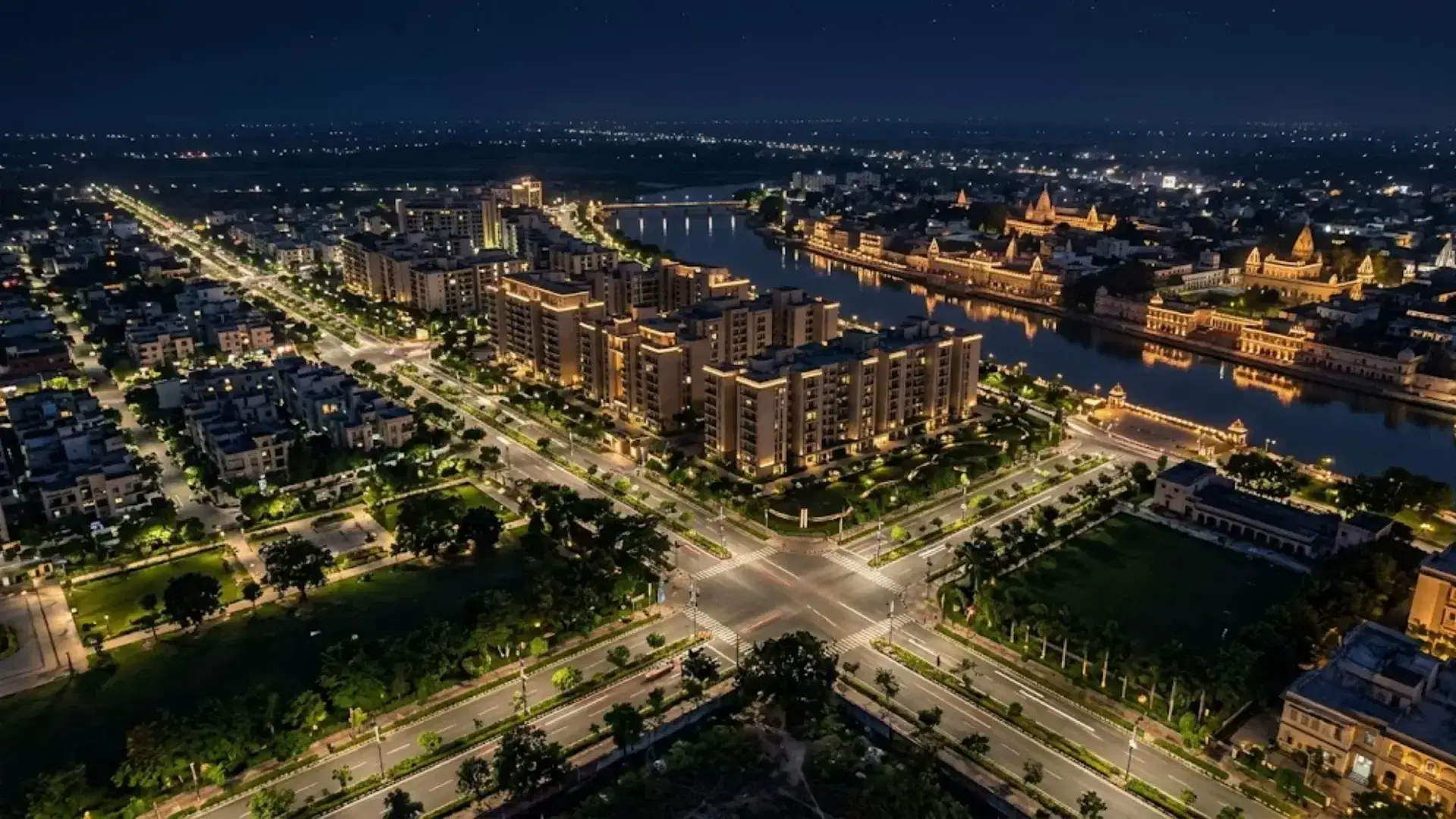 Aerial night view of Ayodhya with illuminated residential developments, wide roads, riverfront areas, and temple architecture.