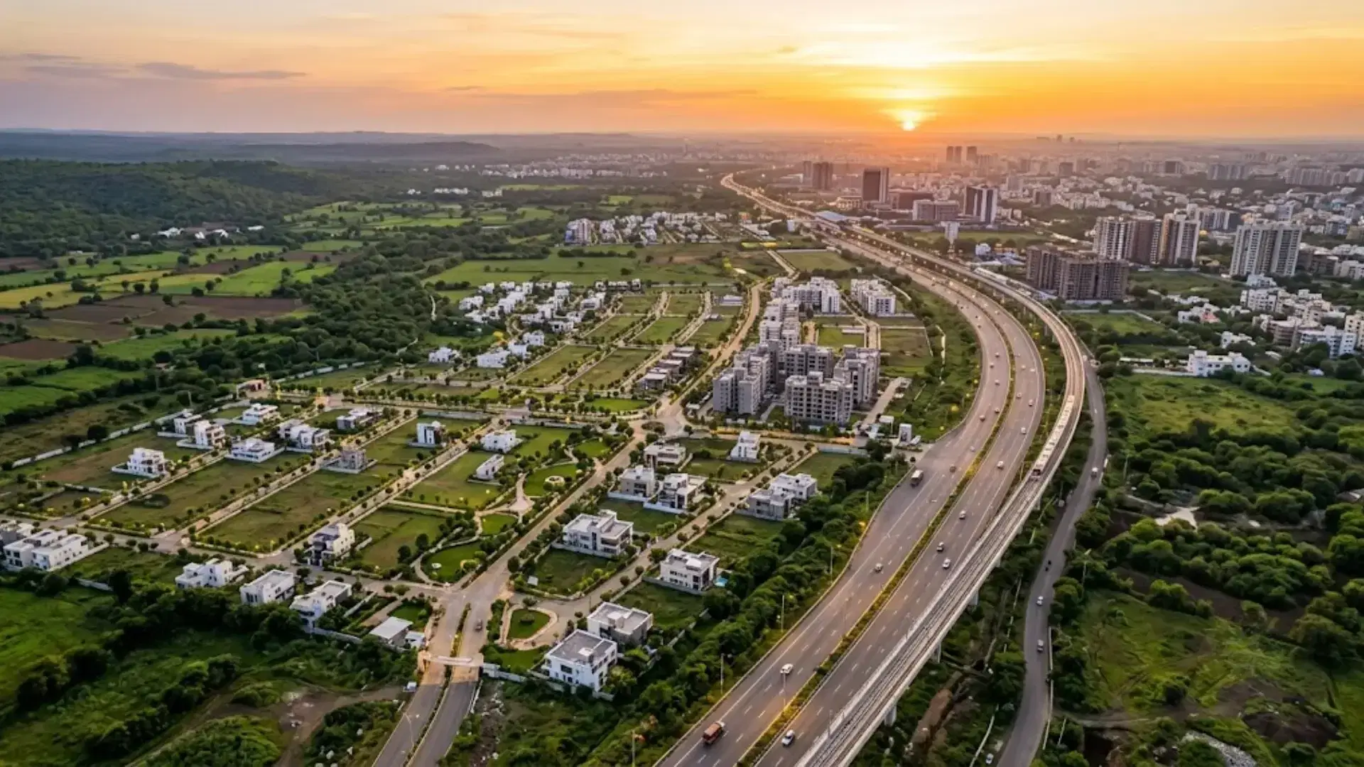 Aerial evening view of a luxury gated villa community in India with landscaped roads, illuminated homes, clubhouse, swimming pool, and central water feature.
